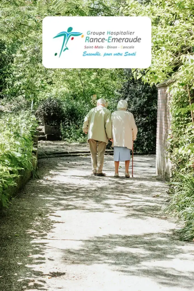 Deux personnes âgées marchent bras dessus bras dessous sur un sentier ensoleillé et bordé d'arbres, illustrant les bienfaits apaisants de la sophrologie en EHPAD à Saint-Malo. En haut de l'image, on aperçoit le logo du Groupe Hospitalier Rance-Emeraude.