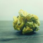 Un morceau de papier jaune froissé, sur lequel figure un texte écrit à la main, repose sur une surface sombre et lisse, devant un arrière-plan clair et flou.