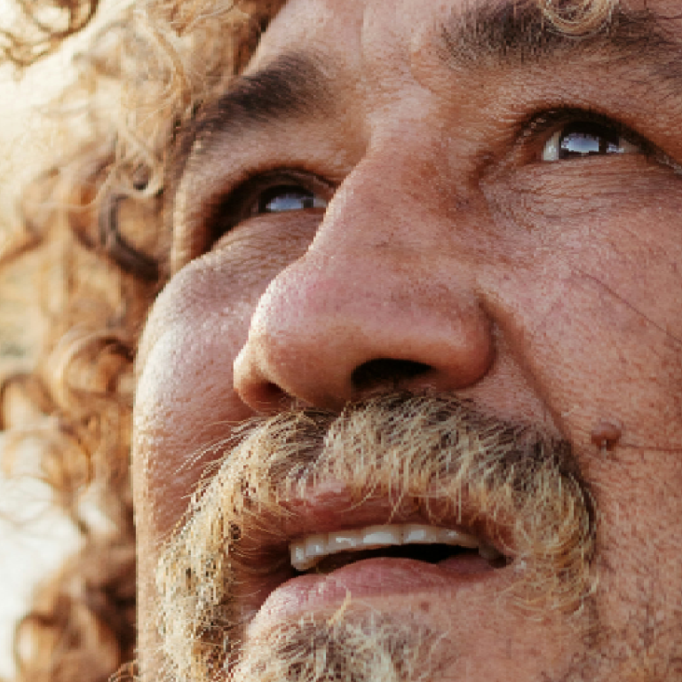 Gros plan sur un homme d'âge mûr aux cheveux bouclés et à la barbe, le regard tourné vers le haut, l'air pensif ; l'arrière-plan légèrement flou crée une atmosphère introspective.